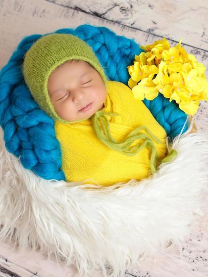 A lovely color combination of yellow, green, and blue makes this newborn portrait bright and happy. The baby is nestled in a soft, fluffy basket.