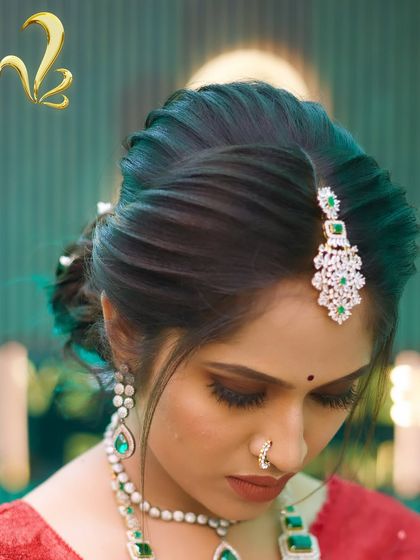 This image highlights the elegant hairstyle created for the reception look. A textured, twisted bun is adorned with a diamond and emerald maang tikka, showcasing how hairstyling is a crucial element of the total look curation I provide.