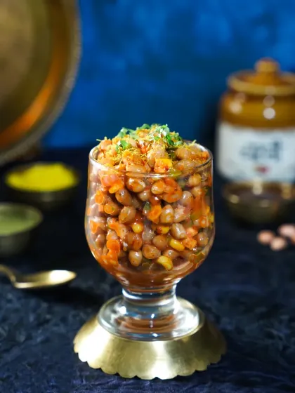 A glass of peanut and corn chaat, elegantly presented in a stemmed glass. The elevated presentation and moody lighting give this simple street snack a sophisticated twist.