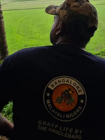 A BMR member in our official club t-shirt, looking out over a serene green landscape. This captures the quiet moments of reflection that are also a part of our riding culture.