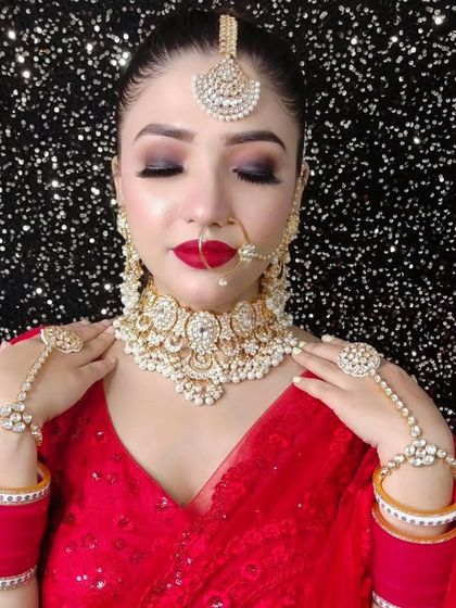 A bride in a vibrant red saree or lehenga, adorned with a beautiful pearl and Polki choker set. The look is completed with a matching hathphool and a simple nath.