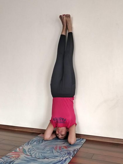 A student holds a supported headstand against the wall. This variation of Sirsasana is excellent for safely experiencing the benefits of inversions, such as improved circulation and focus.