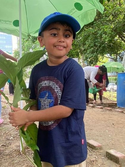A young boy holds a native sapling, ready to plant it and contribute to the restoration of Aravali Creek.