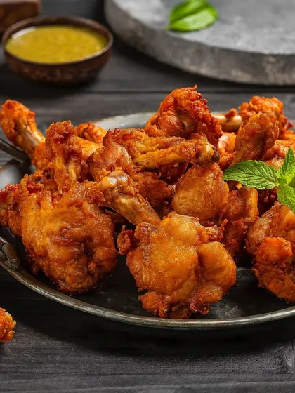 Crispy fried chicken lollipops for Nazeer Foods. The dark, textured background and focused lighting make this a powerful image for a restaurant menu's appetizer section.
