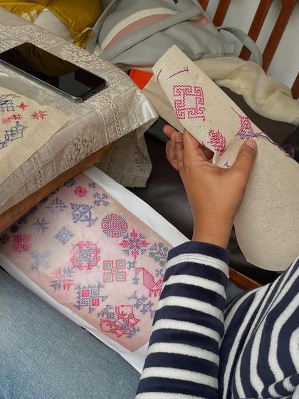 A student referring to a pattern sheet while working on her sampler. We provide all the materials and guidance needed to help you succeed.