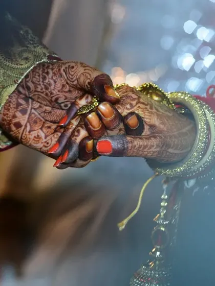 An intimate close-up of the bride and groom holding hands, symbolizing their union and showcasing the bride's mehendi.