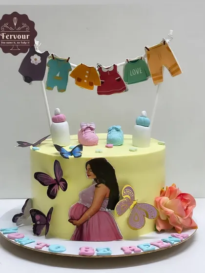 A sweet baby shower cake with a clothesline of baby clothes as a topper. This mixed fruit cake is decorated with butterflies and a beautiful image of a pregnant mother.