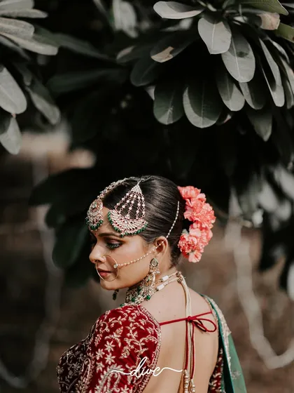 A beautiful shot of the bride's back, showcasing her intricate hairstyle adorned with fresh flowers and the stunning design of her blouse.