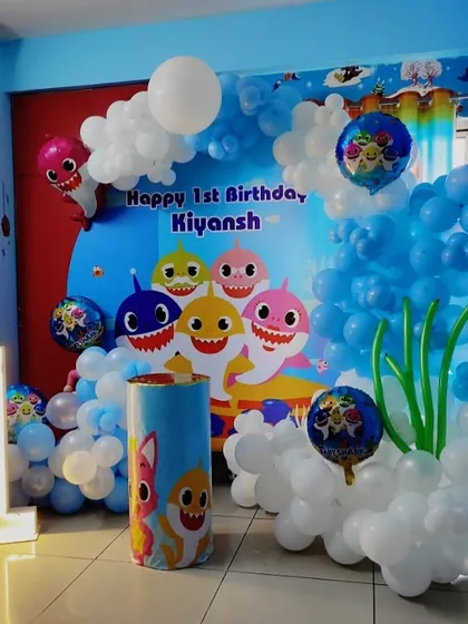 An underwater adventure with this Baby Shark theme for a first birthday. The setup includes a custom backdrop with the Baby Shark family, blue and white balloons to create a bubbly effect, and a light-up number "1".