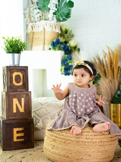 A classic first birthday portrait. This little one sits on a jute pouf next to wooden "ONE" blocks in a warm, earthy-toned studio setup.