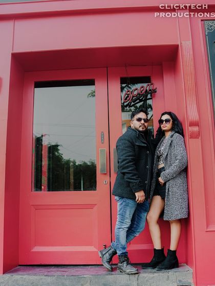 A stylish, full-length shot of a couple posing against a bright pink door, giving off a modern and fashionable vibe.