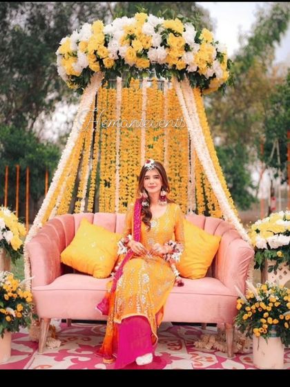 A bride seated at her Haldi ceremony. The backdrop is a beautiful arrangement of yellow flowers and hanging garlands, creating a perfect photo moment.