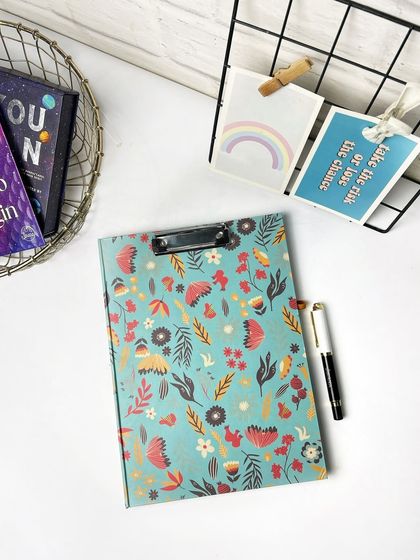 A clean, bright flatlay of a floral clipboard with a pen, styled with other desk accessories. This is a great shot for a product listing on an e-commerce site.