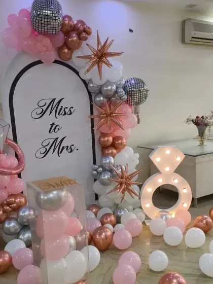 A stunning "Miss to Mrs." decor setup for a bachelorette party or bridal shower. This arch with pink, silver, and rose gold balloons, a marquee ring, and starburst foils is both glamorous and fun.
