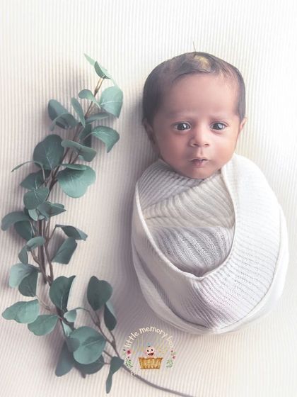 An awake newborn wrapped in white, with a single sprig of eucalyptus for a touch of nature. This is a perfect example of simple, elegant, and modern newborn photography.
