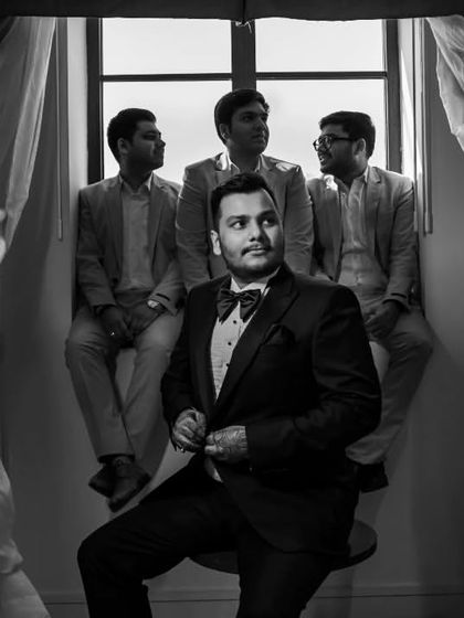 A classic black and white portrait of Roshan and his groomsmen. The composition, with the groom seated and his friends by the window, has a timeless, formal feel.