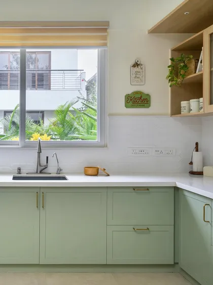 A bright and airy kitchen with sage green shaker-style cabinets and a clean white countertop. The large window allows for plenty of natural light, enhancing the fresh, cottage-like feel.