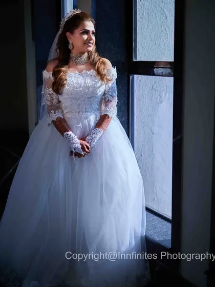 A quiet, contemplative portrait of the bride before her ceremony. The natural light from the window beautifully illuminates her gown and creates a serene, classic bridal shot.