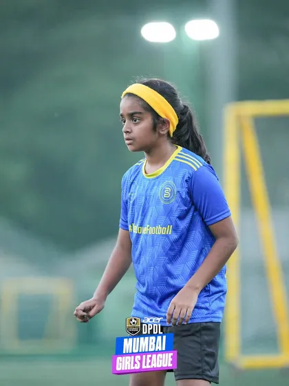 A young girl with a yellow headband shows intense focus and determination during a match. This portrait captures the competitive spirit and passion of our future female stars.