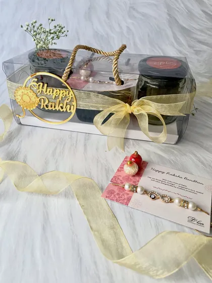 This is our thoughtfully curated Rakhi Indulgence Hamper. It comes in a clear, easy-to-carry box and includes jars of coffee chocolate cookies and mini brownies, a beautiful Rakhi, a heartfelt note, and traditional kumkum chawal for the ceremony.