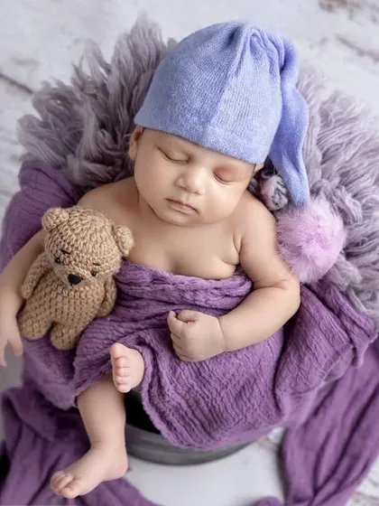 Cuddling a tiny teddy bear, this baby boy is wrapped in purple and looks so cozy.