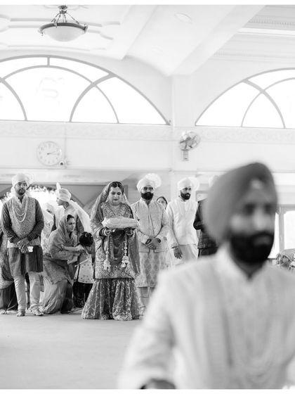 A creative shot of the bride during the Anand Karaj, framed by the groom in the foreground. This composition adds depth and a sense of perspective to the scene.