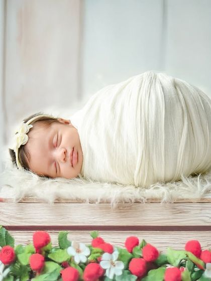 A sweet and simple strawberry-themed portrait. The baby is wrapped in white and rests on a crate surrounded by a wreath of strawberries.