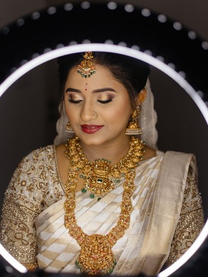 A close-up of the bride, framed by a ring light. Her makeup is flawless, and her white and gold saree looks ethereal.