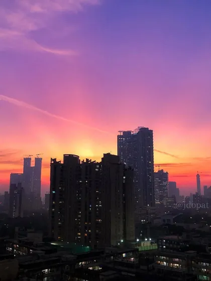 A vibrant purple and pink sunset creates a beautiful backdrop for the silhouetted buildings of Mumbai.