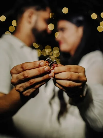 A romantic, moody shot of the couple holding their rings, with a beautiful bokeh of fairy lights in the background. The focus is on the rings, symbolizing their commitment in a creative and artistic way.