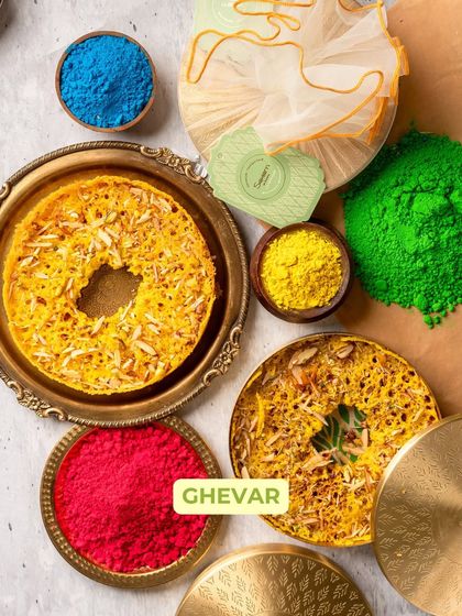 A top-down view of my festive Ghevar, surrounded by vibrant Holi colours. This disc-shaped sweet is a traditional favourite, perfect for gifting in its elegant brass box.
