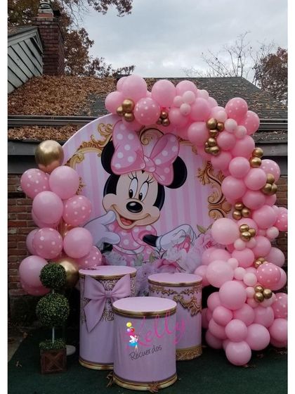 A pink and gold Minnie Mouse theme with elegant pedestals for the cake and treats, framed by a beautiful balloon arch.