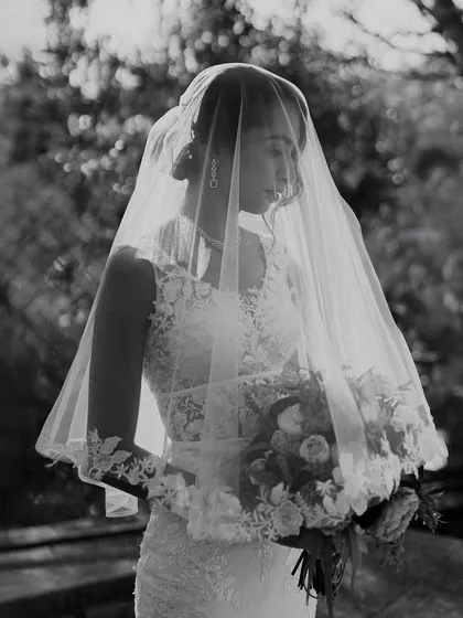 A timeless black and white portrait of a bride in her veil, holding her bouquet. The soft, natural light and her serene expression give this image an ethereal and classic beauty.