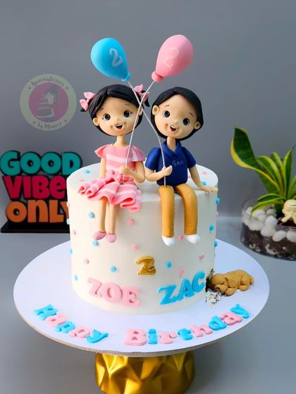 A sweet cake for twins Zoe and Zac, featuring custom figurines of the siblings holding balloons.