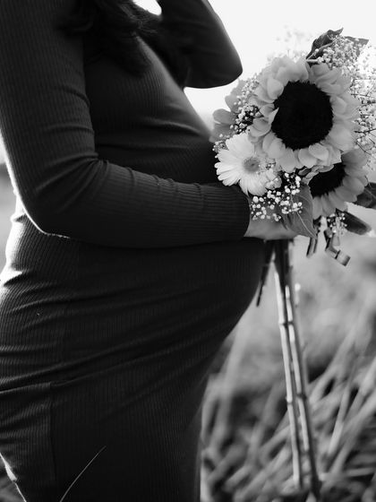 A beautiful black and white close-up of the mom-to-be holding a bouquet of sunflowers against her bump. The lighting and composition are artistic and timeless.