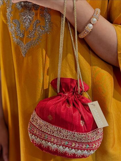 A classic red potli with a delicate silver embroidered border, held against a mustard yellow kurta. It's the perfect accessory to add a festive touch.