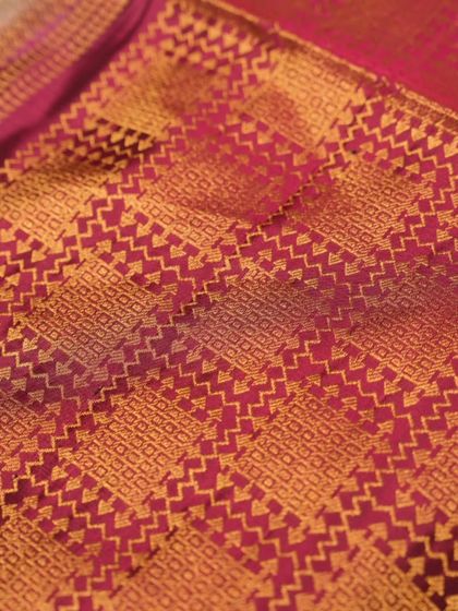 A close-up of a complex geometric pattern woven in gold zari on a pink silk base, showcasing the weaver's mathematical precision.