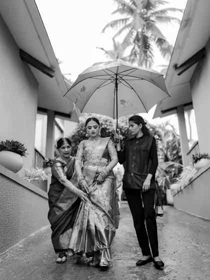 A candid black and white shot of the bride being escorted under an umbrella on a rainy day. It's a real moment, full of care and support.