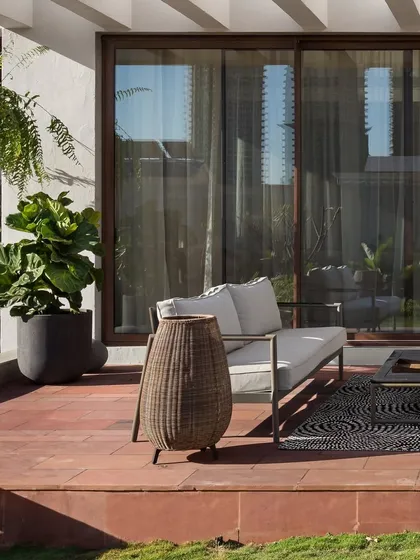 The ground-floor terrace provides a quiet space for relaxation, with comfortable seating and potted plants that enhance the connection to the garden. The red stone flooring adds a warm, earthy element to the design.