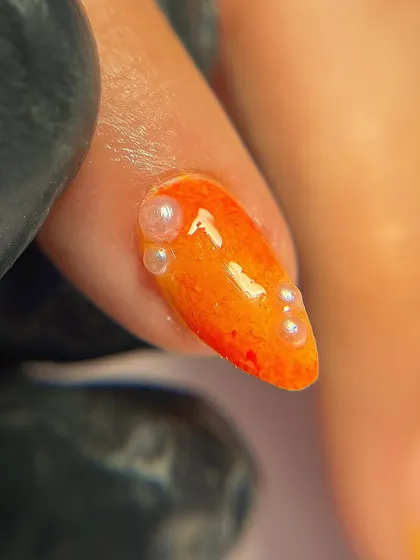 A close-up of the pearl accents on the orange marble nail. These tiny details add a touch of sophistication.