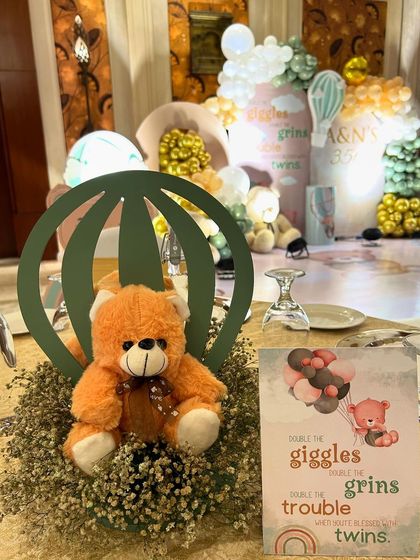 A close up of a table centerpiece for the twins' teddy bear party. It features a cute teddy bear in a hot air balloon cutout, surrounded by baby's breath flowers.