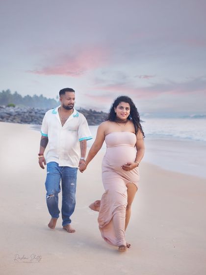 A classic portrait of the couple walking on the beach. The soft sand, gentle waves, and beautiful sky create a perfect, tranquil setting for a maternity photoshoot.