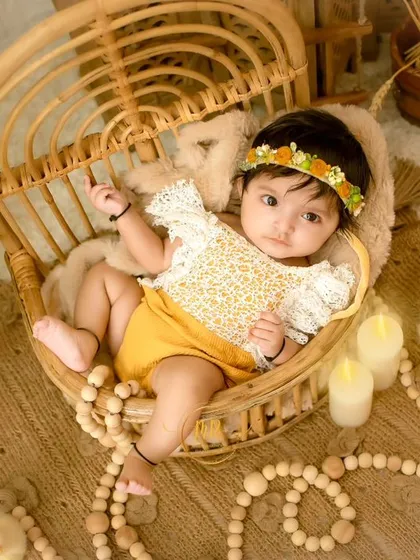 An overhead shot of a baby girl in a wicker chair, looking up curiously at the camera.