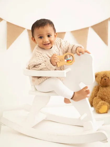 A classic first birthday portrait with a rocking horse and teddy bear. These timeless props create a nostalgic and sweet setting for milestone photos.