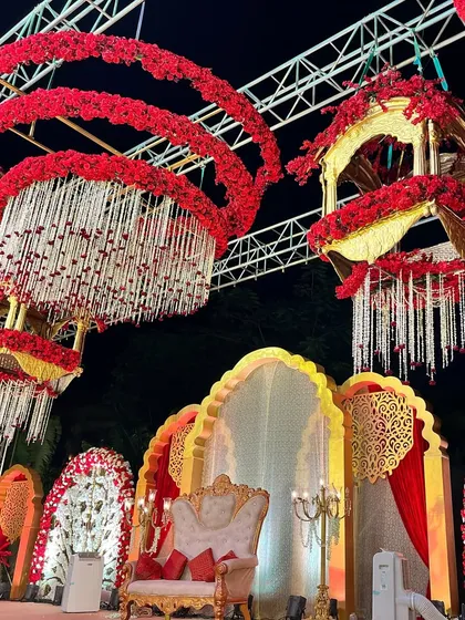 A magnificent wedding stage in red and gold. The hanging floral chandeliers and traditional 'jharokha' style backdrop create a look of pure opulence.