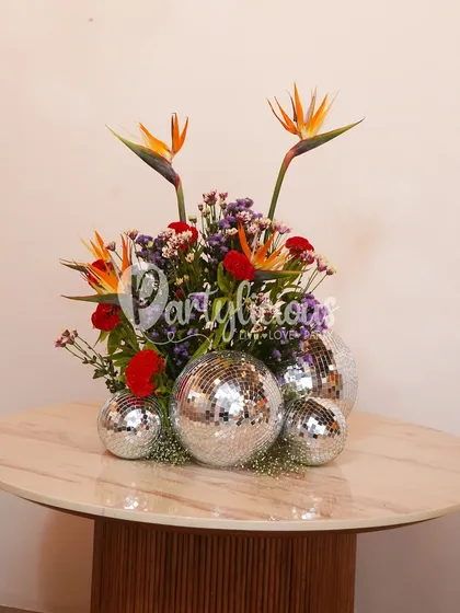 A modern and vibrant floral arrangement featuring Birds of Paradise and red carnations, playfully mixed with sparkling disco balls for a fun, festive touch.