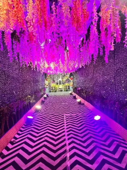 An immersive entrance tunnel designed to create a magical experience for guests. The walkway features a chevron pattern, while the walls are covered in a sparkling texture and the ceiling is adorned with hanging wisteria under purple lighting.
