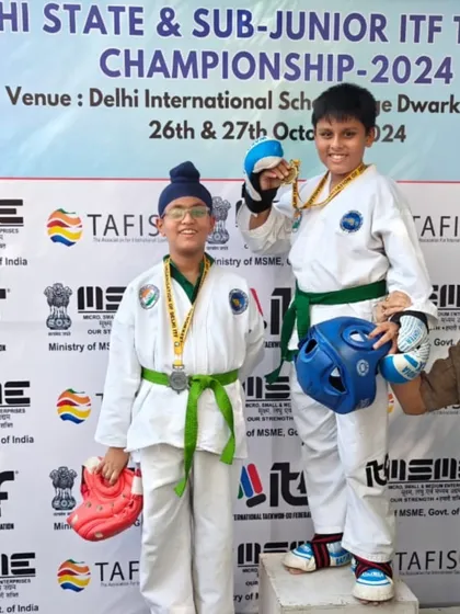 Two young competitors, equipped with full sparring gear, on the podium after their match.