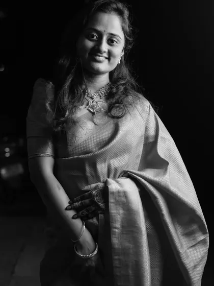 A soft and elegant black and white portrait of a woman in a traditional silk saree, her gentle smile lighting up the frame.