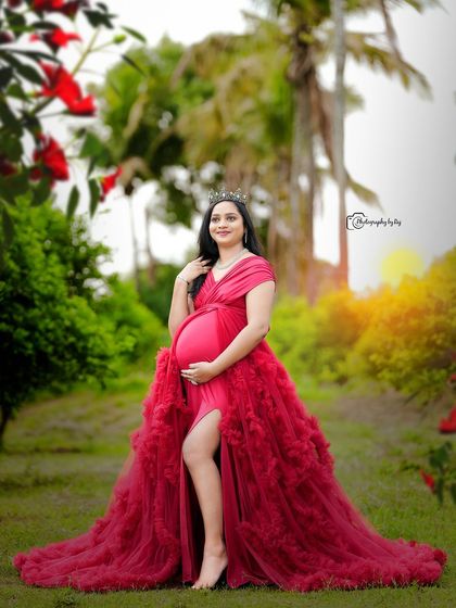 A regal portrait of a mother-to-be in a red ruffled gown and crown, enjoying the beauty of our garden.